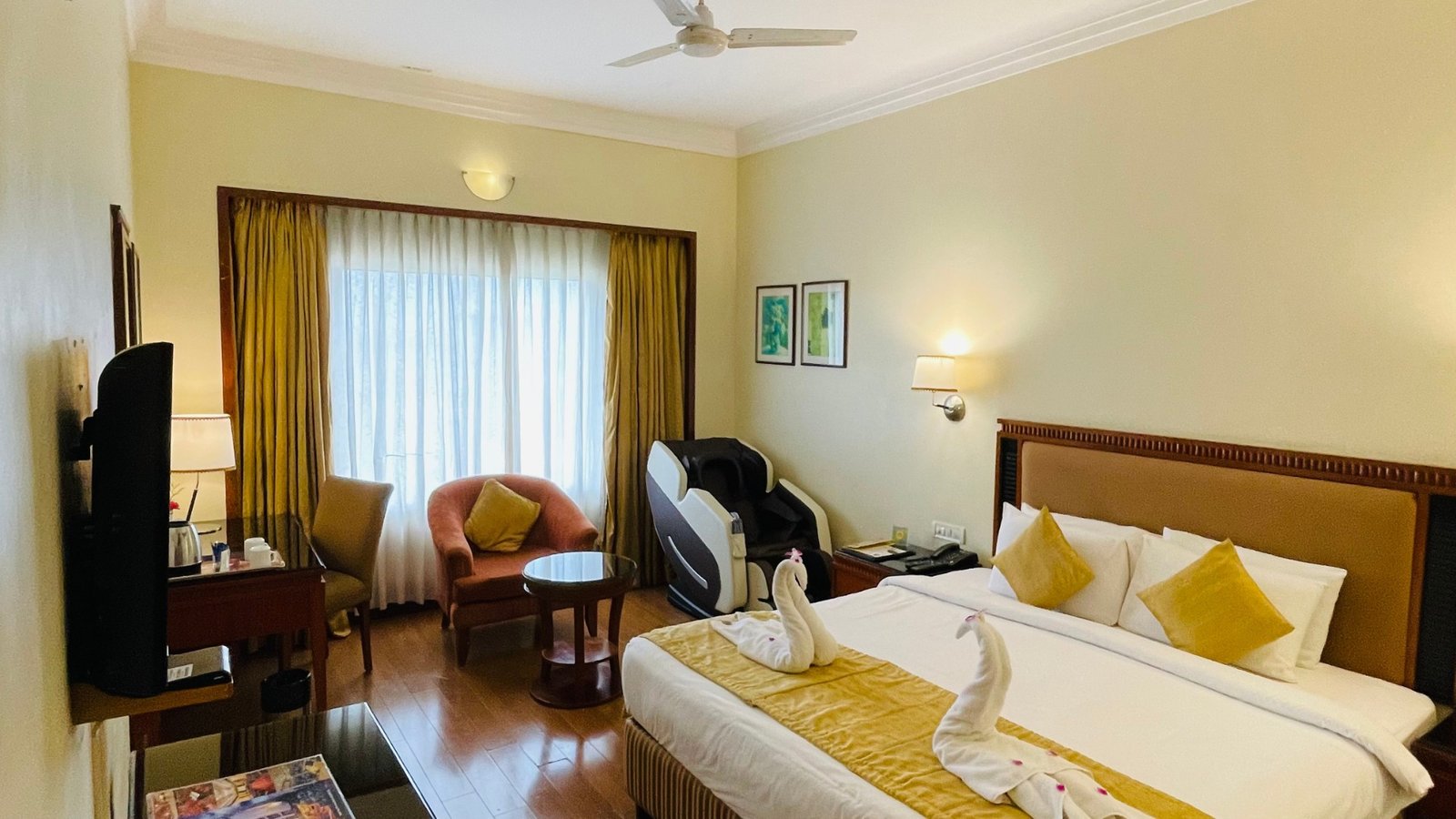Spacious deluxe room at Hotel Royal Court Madurai featuring a king bed, in-room massage chair, cozy seating area, and swan towel art.